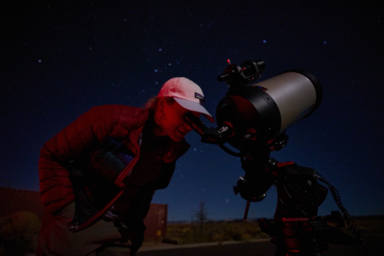 Tour guest with a red headlamp looking through a Celestron telescope eyepiece at night